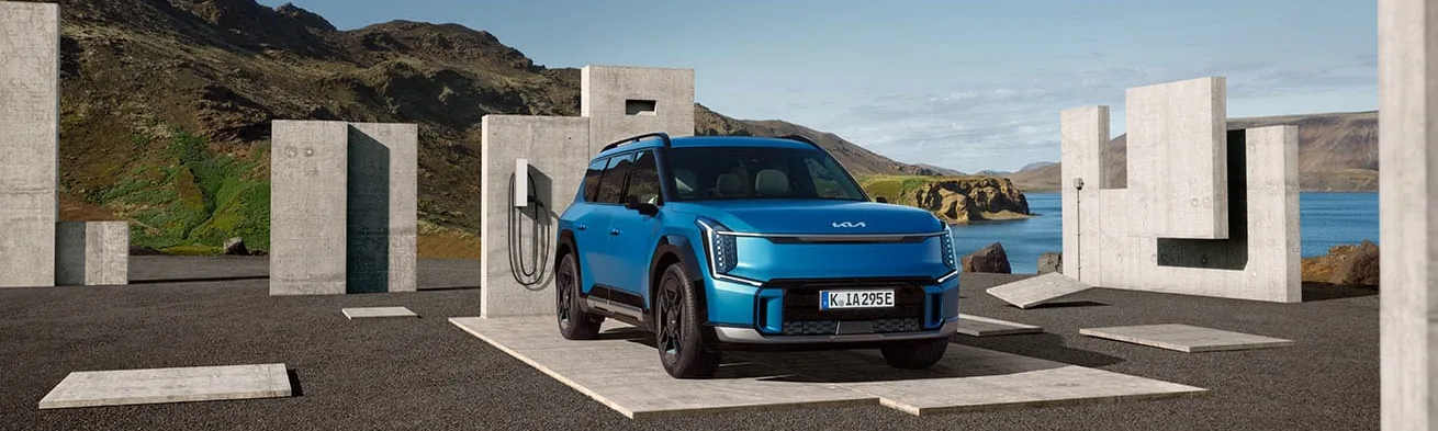 Kia EV9 in Blau an einer Ladesäule vor Küstenlandschaft